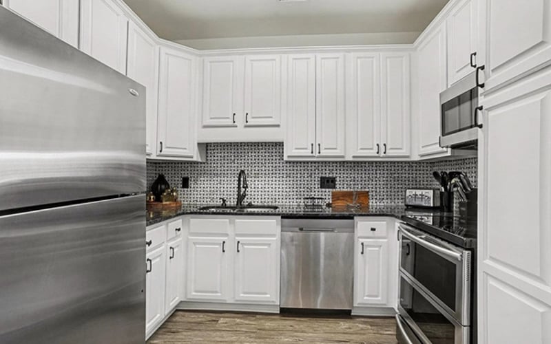 Bright white kitchen with granite counters, dishwasher, and stainless steel appliances